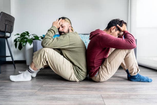 Two men sitting back to back looking distressed, showing disconnection and unresolved conflict