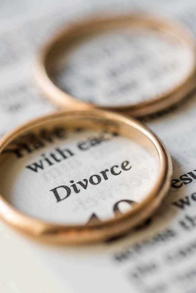 Wedding rings resting on paperwork about divorce, symbolising relationship breakdown, separation, grief, and emotional loss.