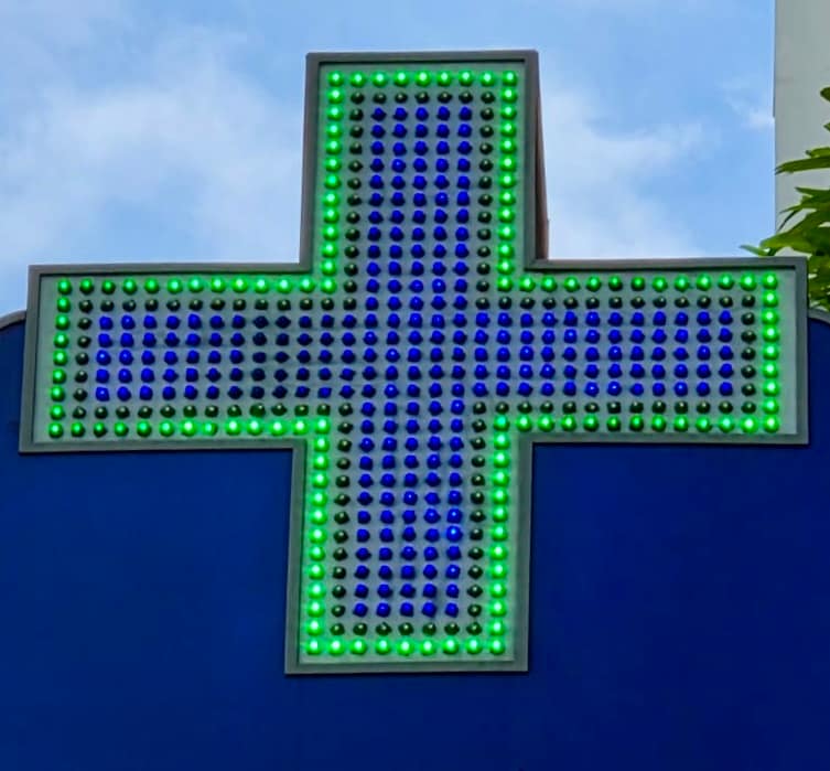 Green medical cross sign with some leaves to the top right